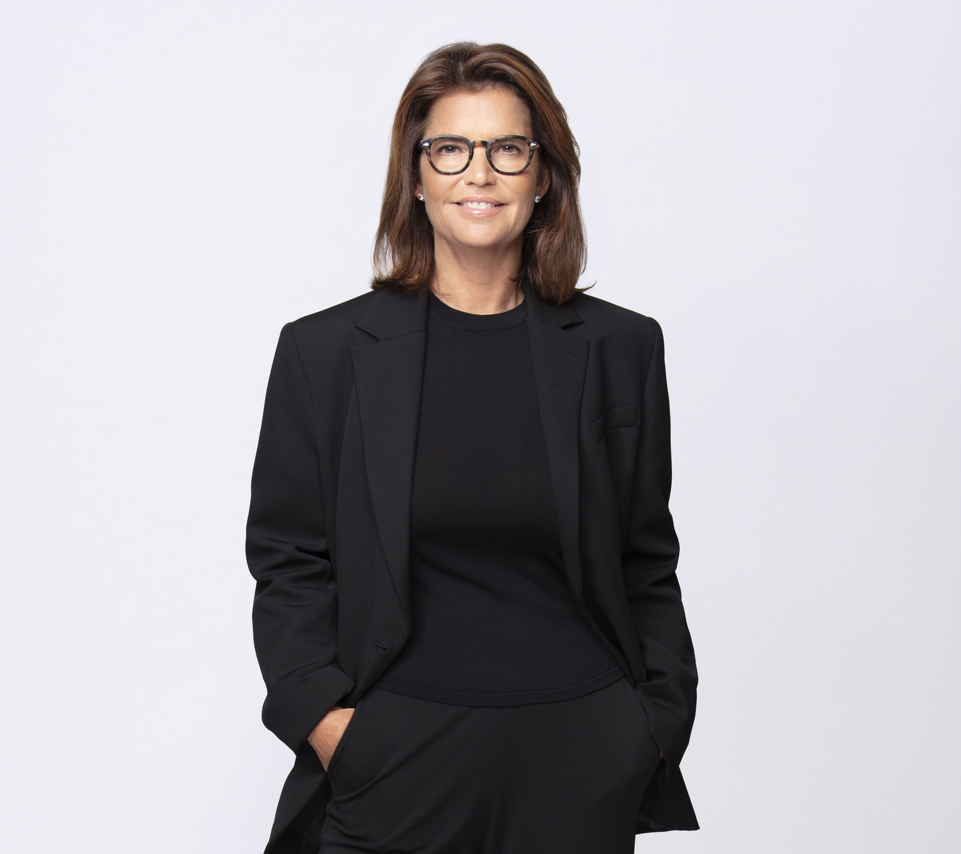 Frau in elegantem schwarzem Anzug mit Blazer und Hosen, lächelt selbstbewusst.