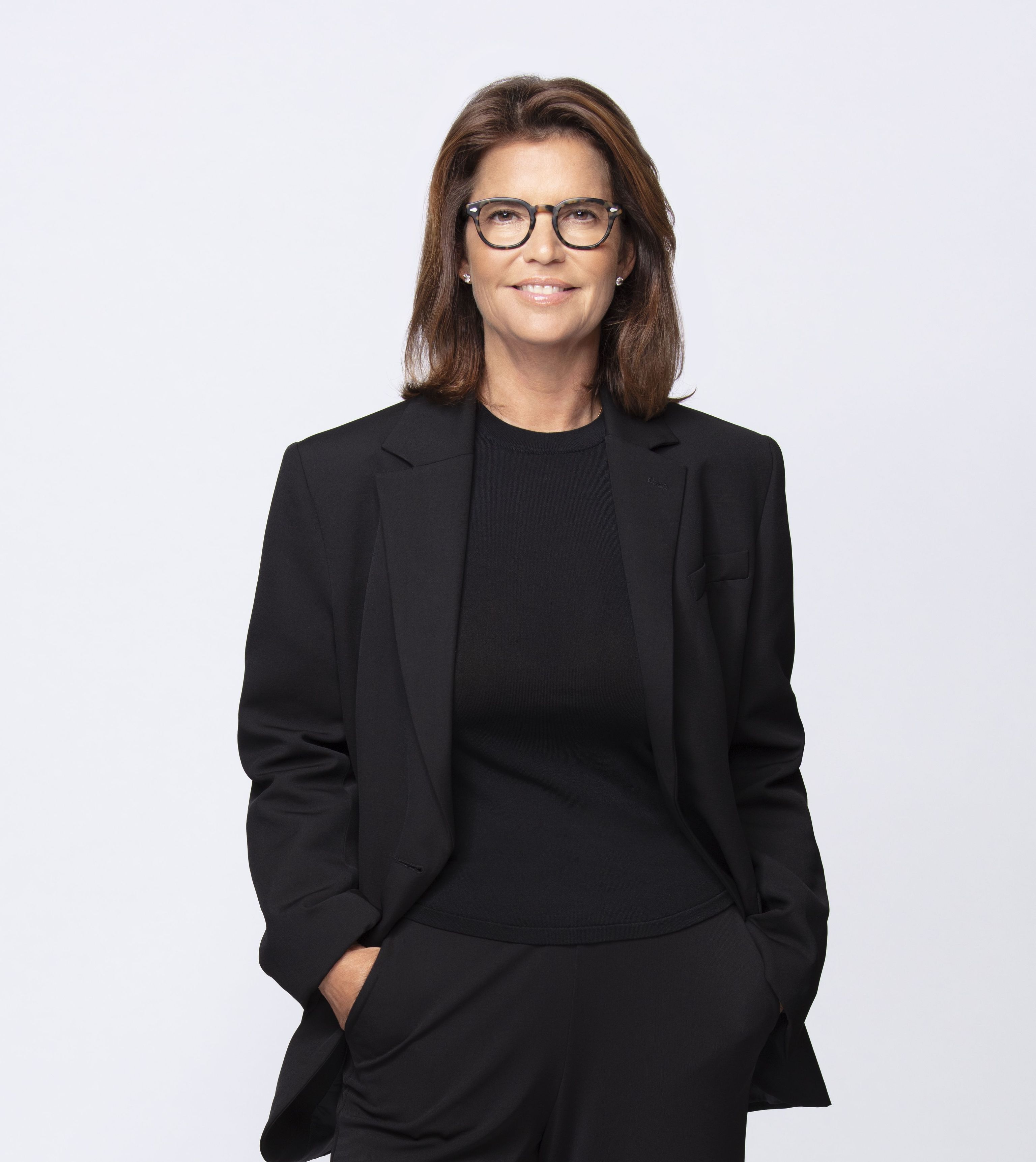 Frau in elegantem schwarzem Anzug mit Blazer und Hosen, lächelt selbstbewusst.