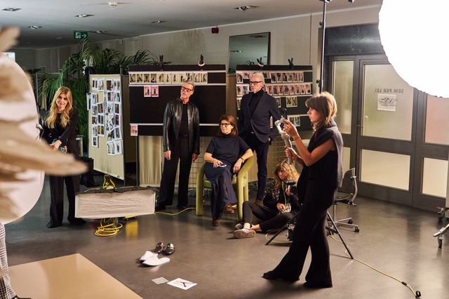 Gruppe von Menschen bei einer Präsentation oder Probe in einem Studio mit Musikinstrumenten und Fotos.