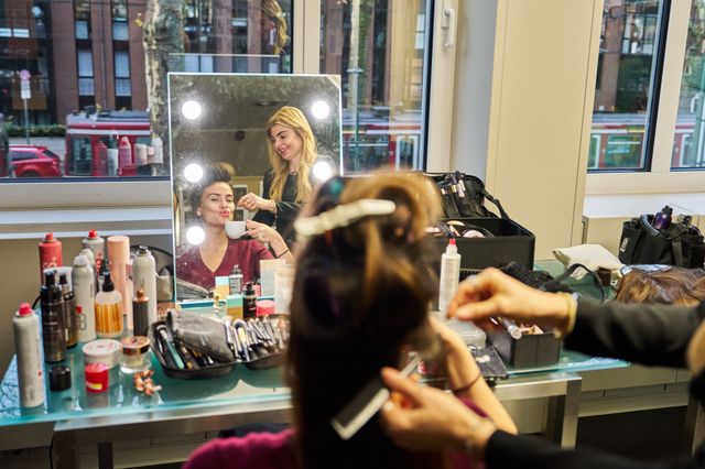 Frau lässt sich im Spiegel Make-up auftragen, Kosmetikartikel auf Tisch.