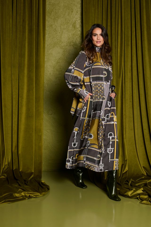 Frau trägt elegantes, gemustertes Langkleid mit goldenen Akzenten und schwarzen Stiefeln.